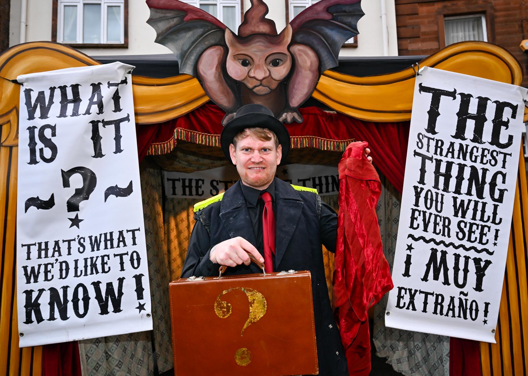 A performer stood in front of a sideshow booth