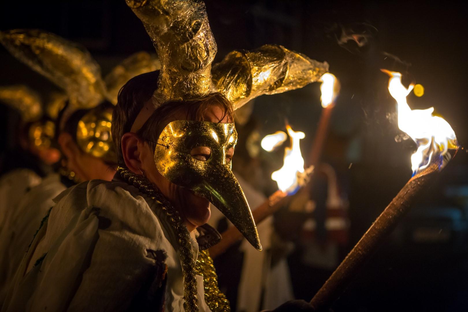 Person in The Winter Droving procession wearing mask with fire torch