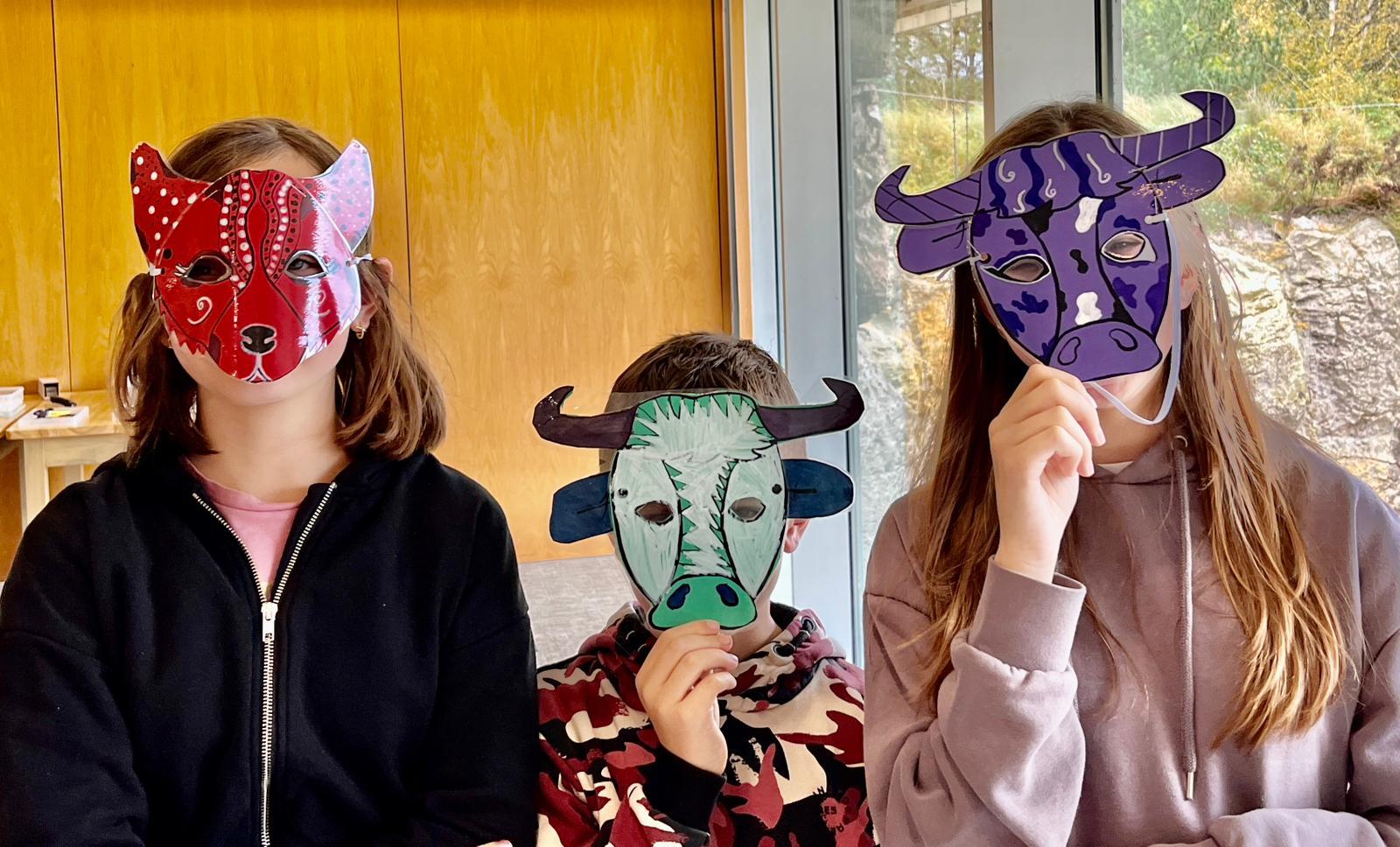 Three children wearing masks made in workshop