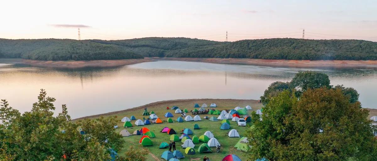 Tents pitched on a grassy lakeshore among trees at sunset, a campground scene like the lakeside gay campgrounds in this guide