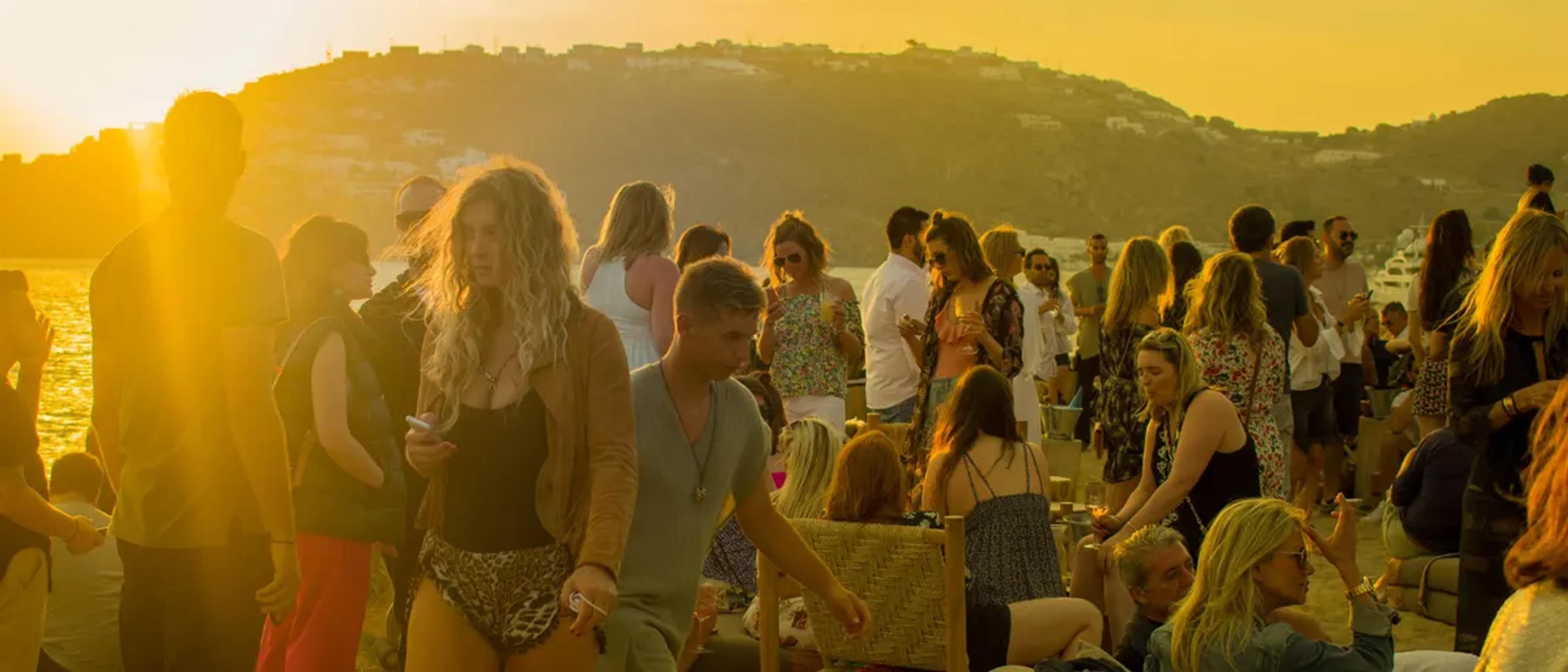Beach party crowd dancing at golden hour beside the water in summer