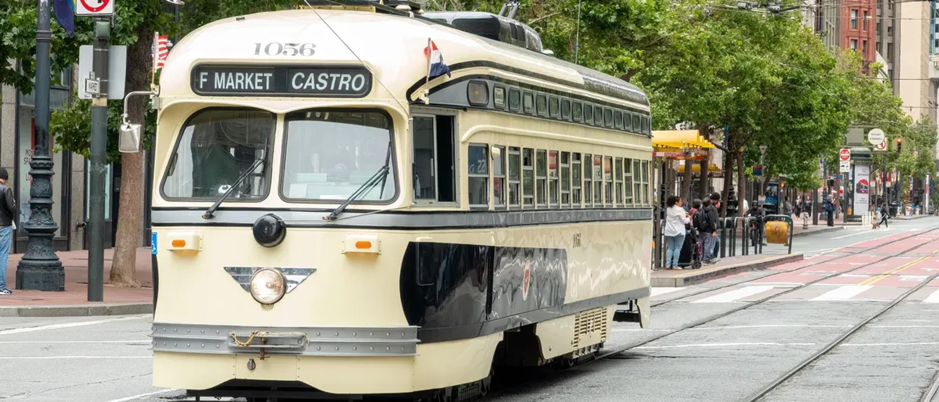 A vintage F Market & Castro streetcar on Market Street in San Francisco, with a rainbow flag on a lamppost