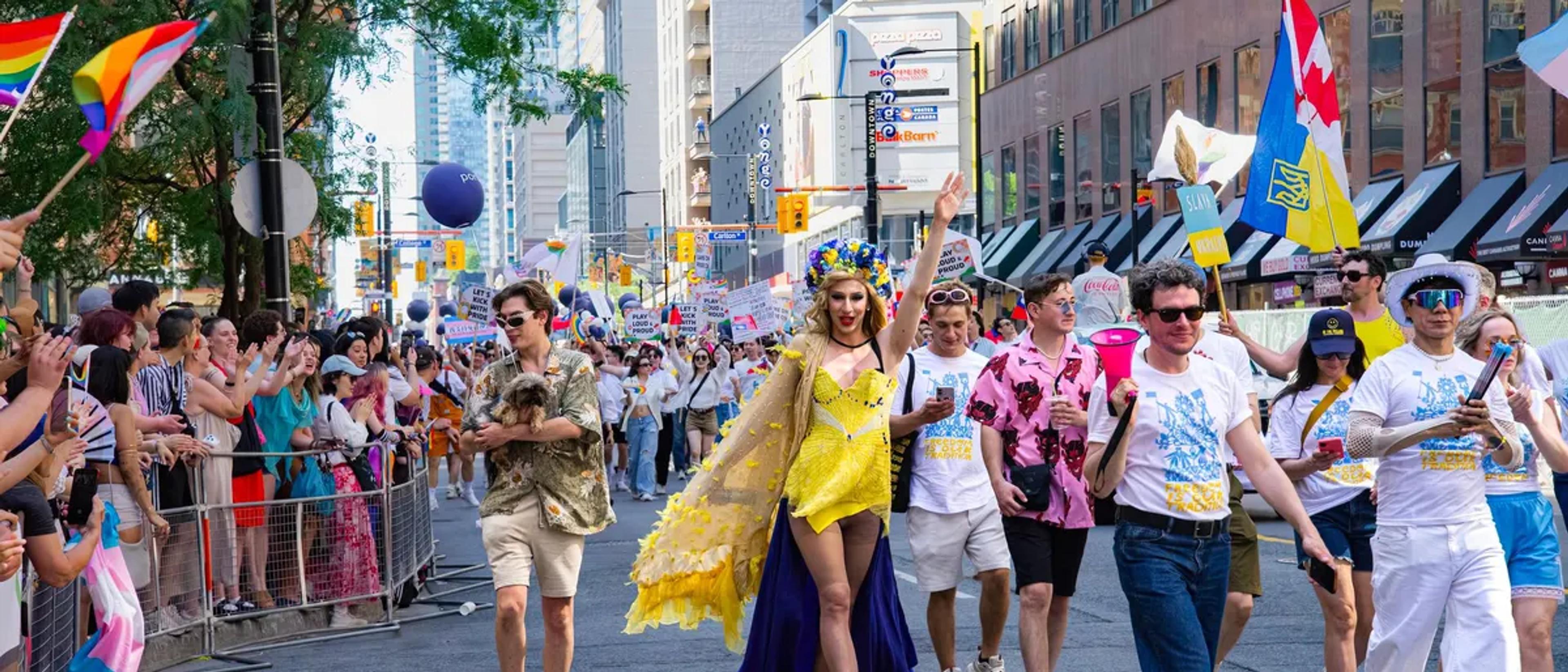 Dancers and crowds fill a downtown street during a large Pride parade
