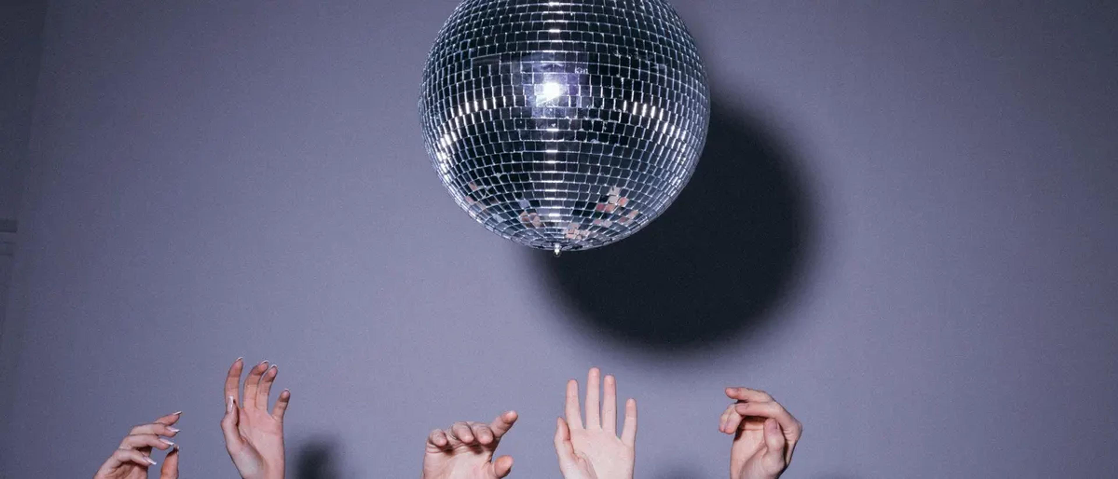 Hands reaching up toward a mirrored disco ball