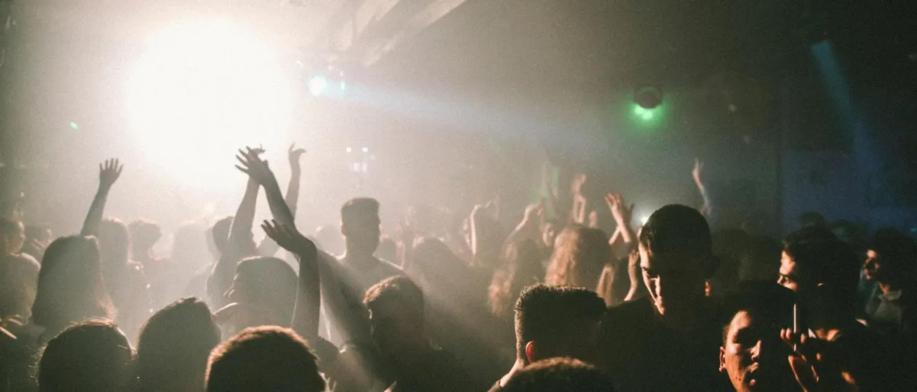 Dense nightclub dance floor crowd with hands in the air amid hazy warm light