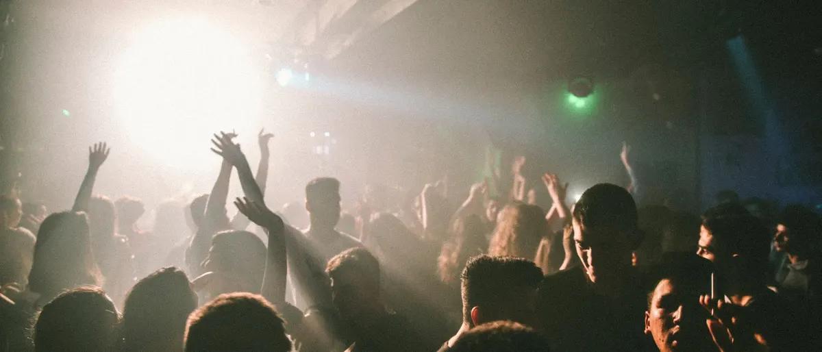 Dense nightclub dance floor crowd with hands in the air amid hazy warm light