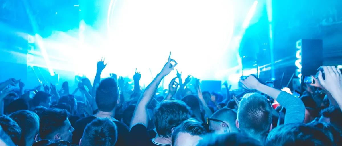 Nightclub crowd dancing with hands raised under bright blue laser lights at a New Year's Eve circuit party