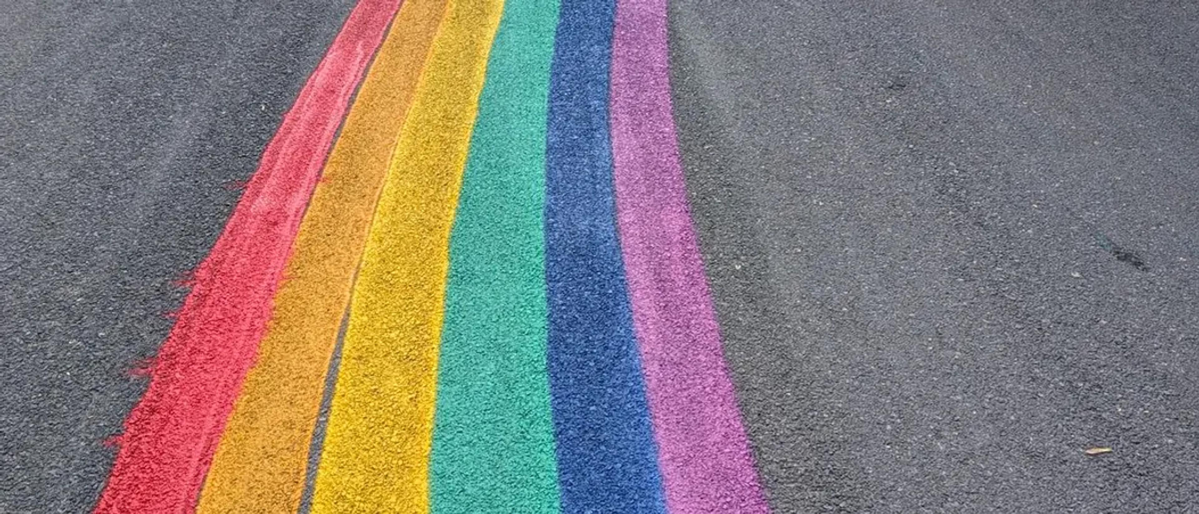 A rainbow-painted Pride crosswalk running across a city street
