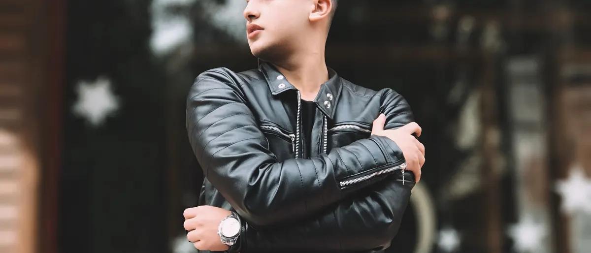 Man in a black leather biker jacket standing with arms crossed