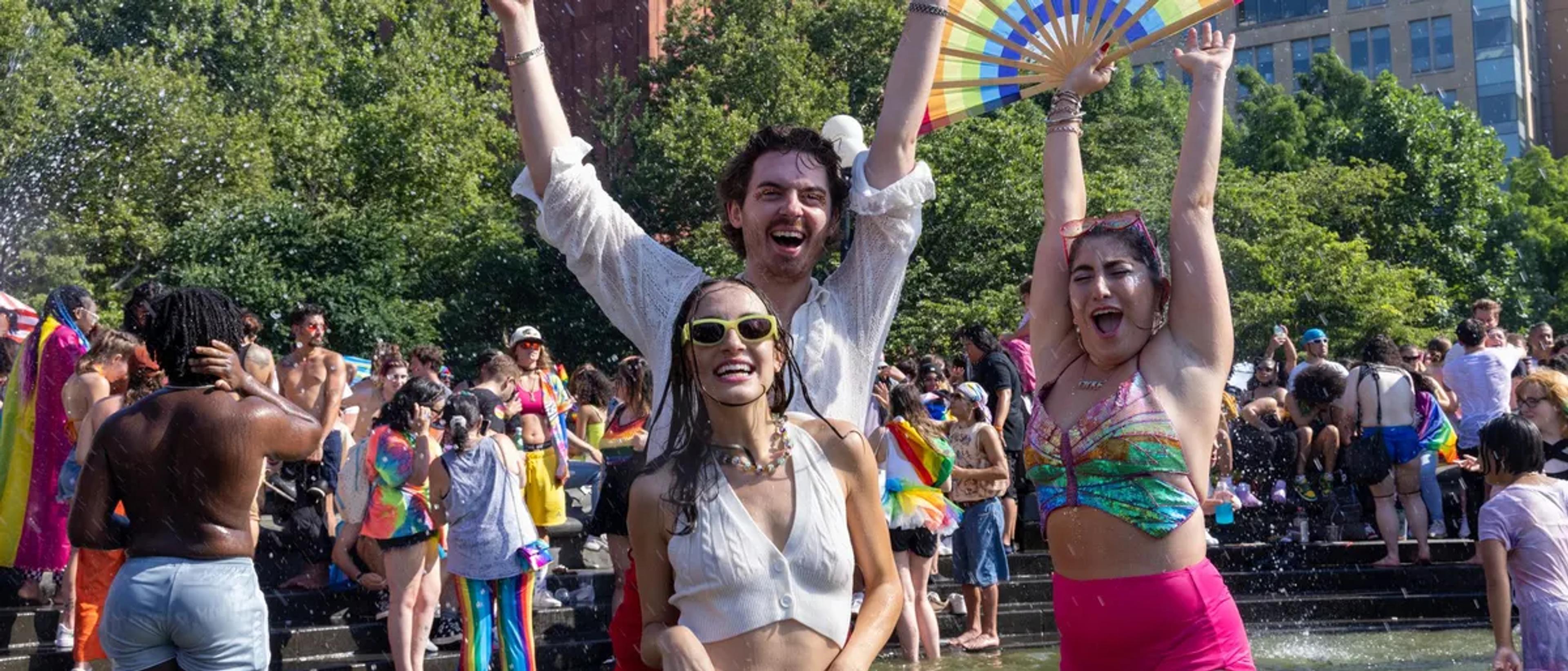 Friends dancing with arms raised at a sunny outdoor Pride celebration