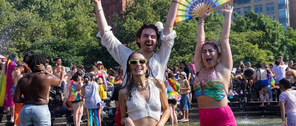 Friends dancing with arms raised at a sunny outdoor Pride celebration