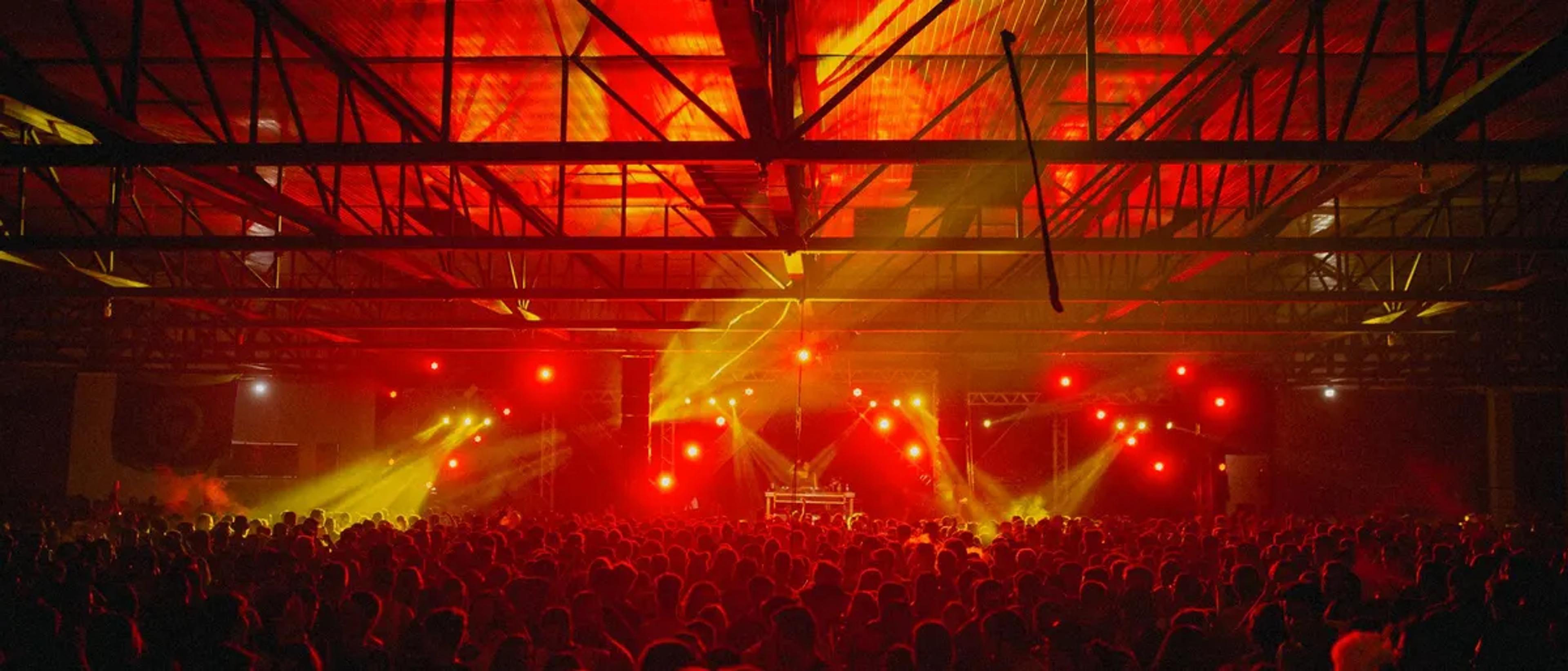 Huge festival crowd in front of a stage bathed in red and gold lights