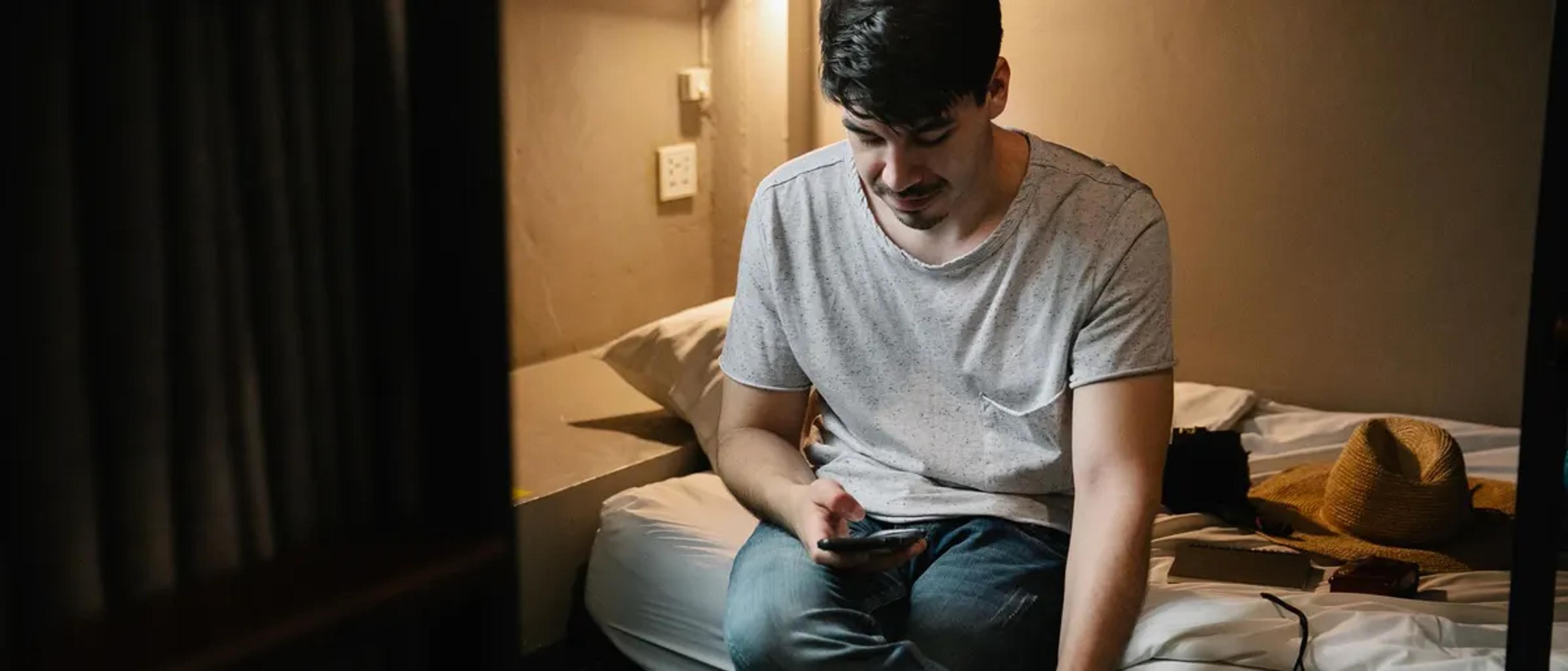 A man sitting on a hotel bed looking at his phone