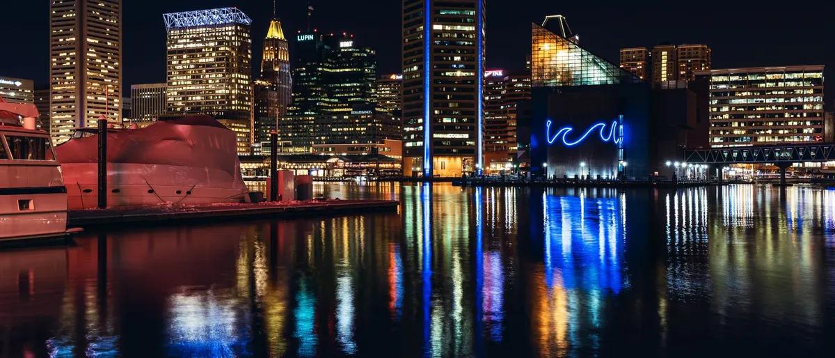 Baltimore's Inner Harbor skyline lit up at night, its colored lights reflected in the water