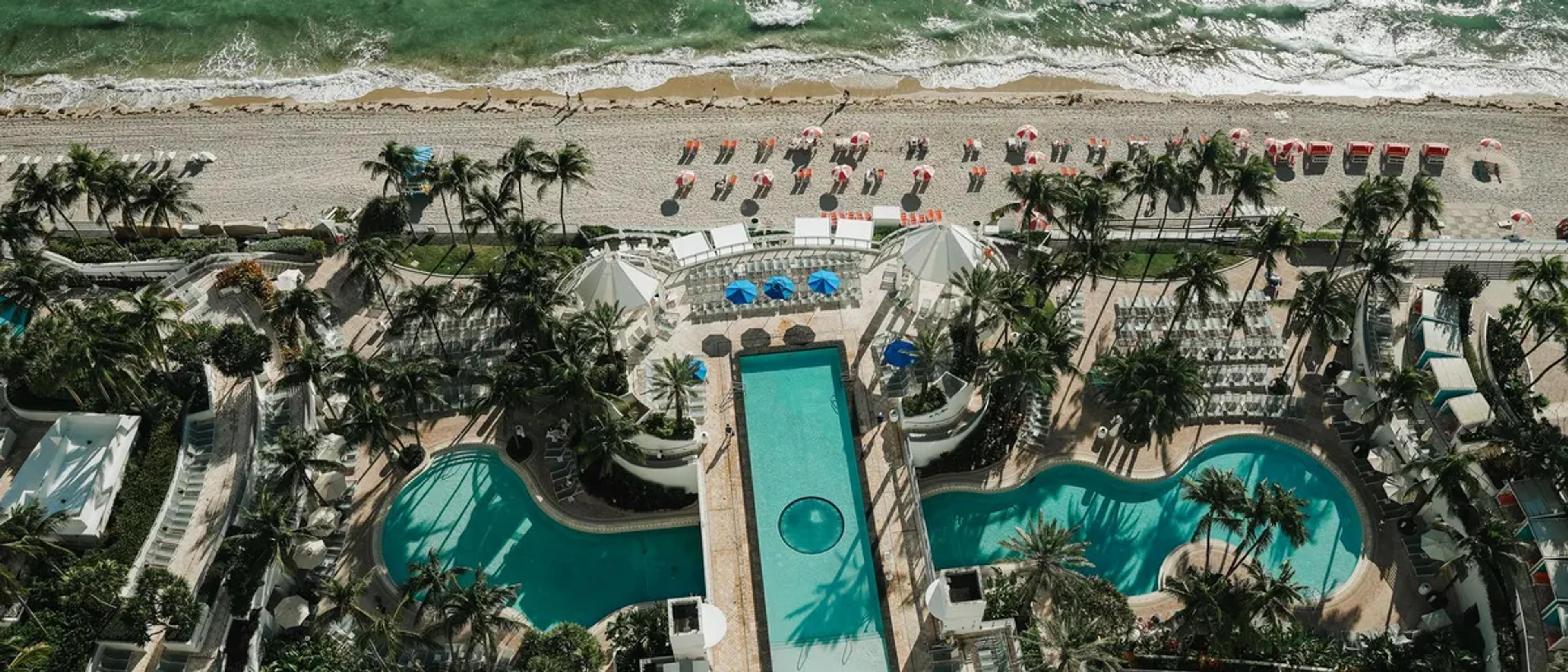 Aerial view of a beachfront resort pool deck with palm trees and the Atlantic beach beyond in Fort Lauderdale