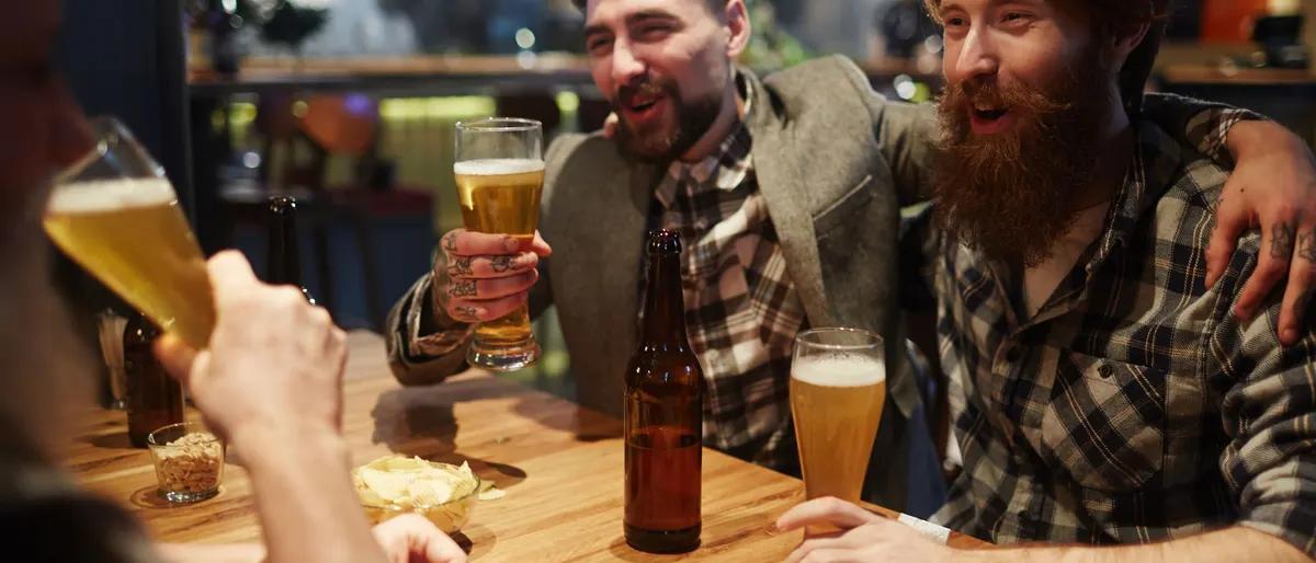 Group of burly bearded men toasting glasses of beer together in a warm pub