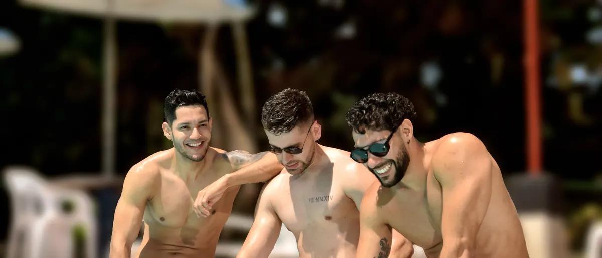 Three men in swim trunks laughing together at the edge of a hotel pool