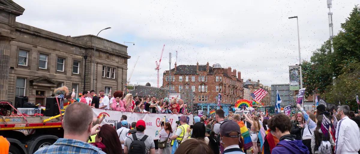 A wide city street filled with revelers and rainbow colors during a Pride celebration