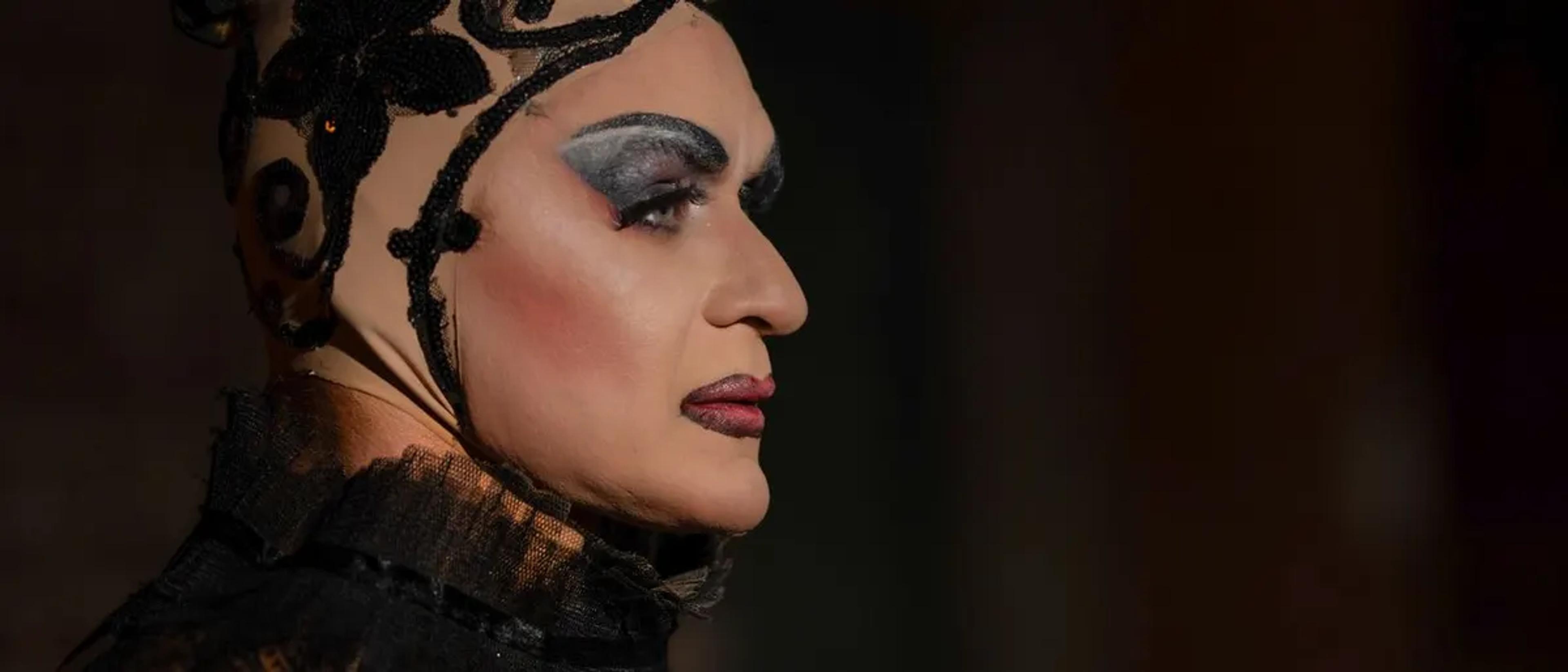 Dramatic profile of a drag performer with bold silver makeup under moody stage lighting