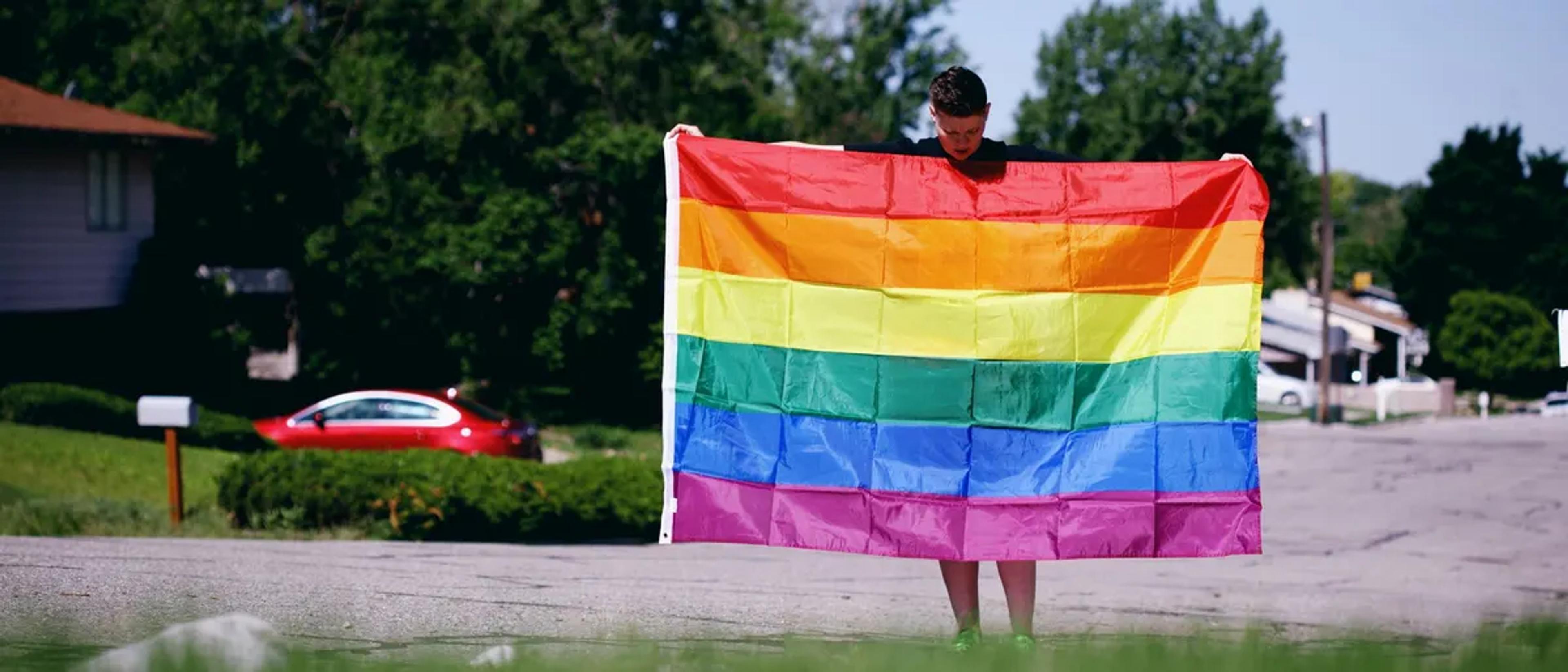 Person holding a rainbow Pride flag on a residential street