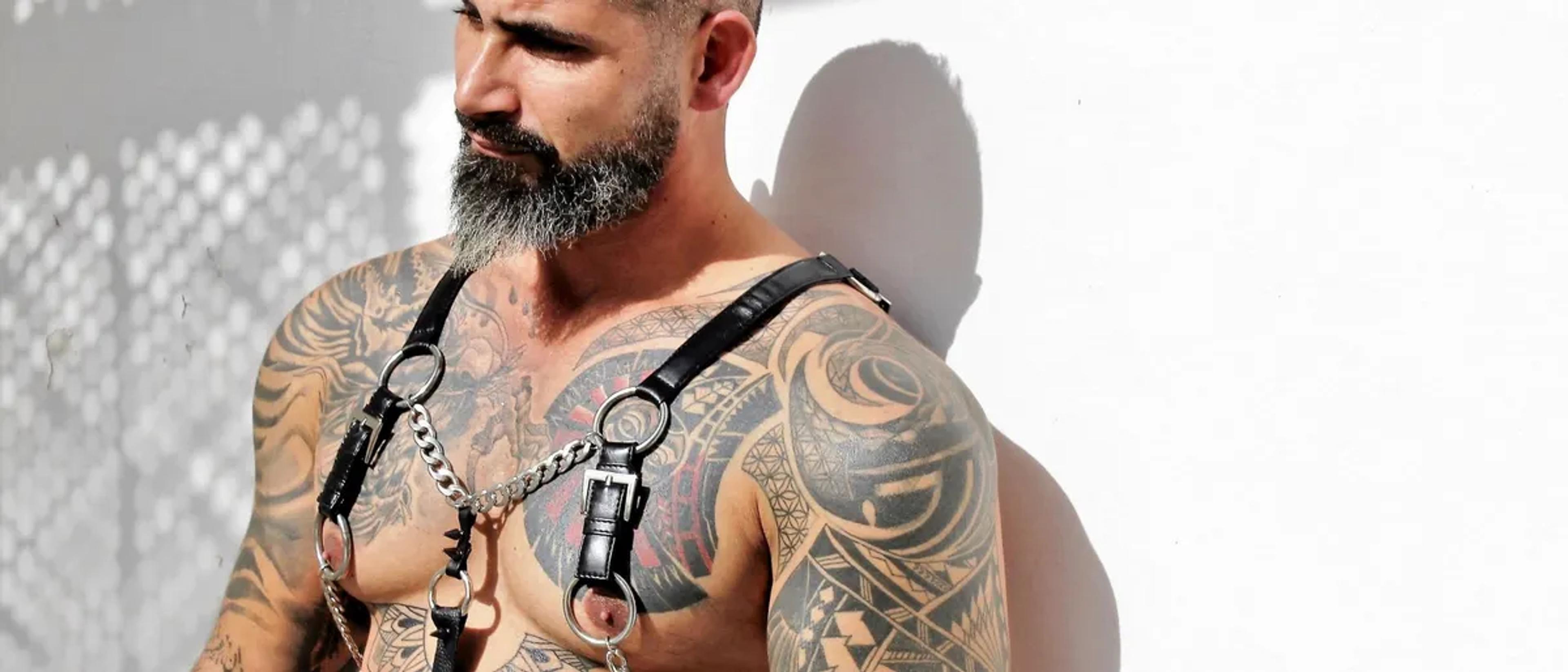 Tattooed bearded man wearing a black leather chest harness