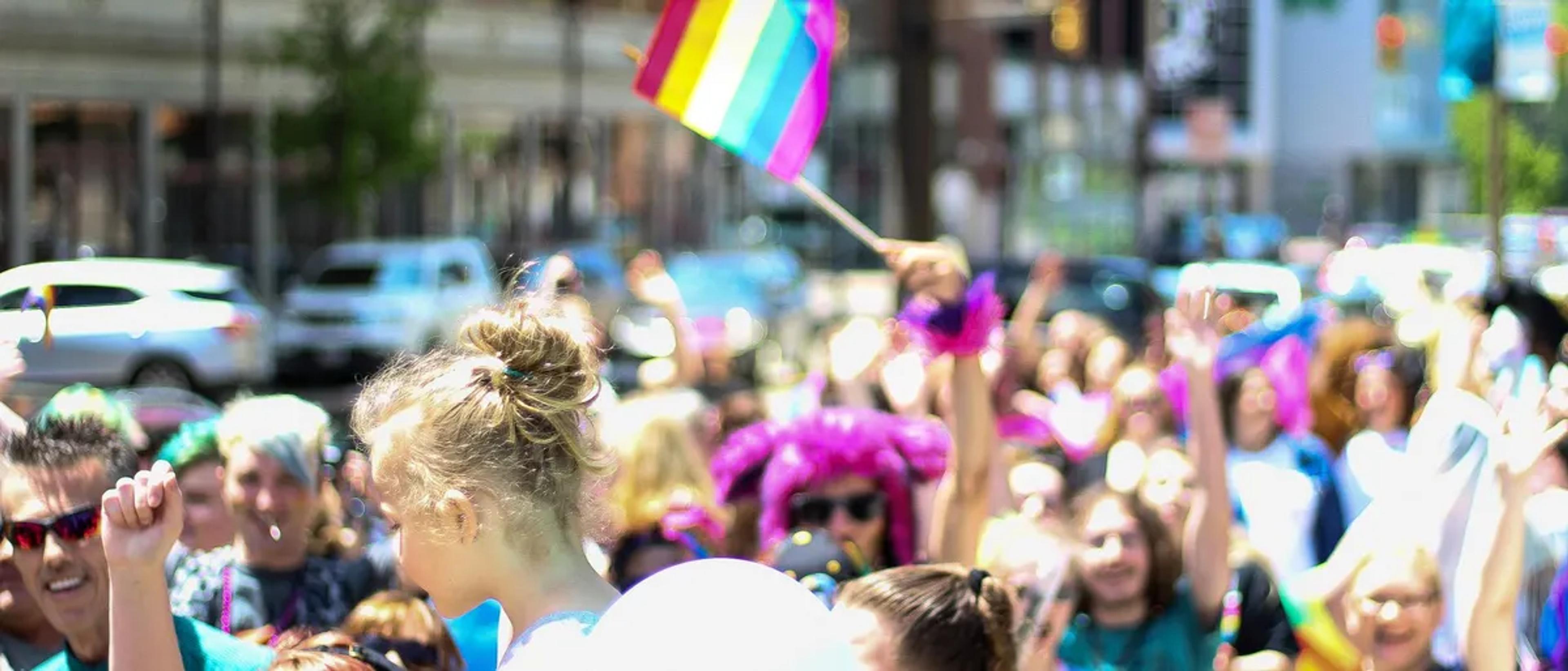 Festival-goers raising a rainbow flag amid a colorful Pride street crowd