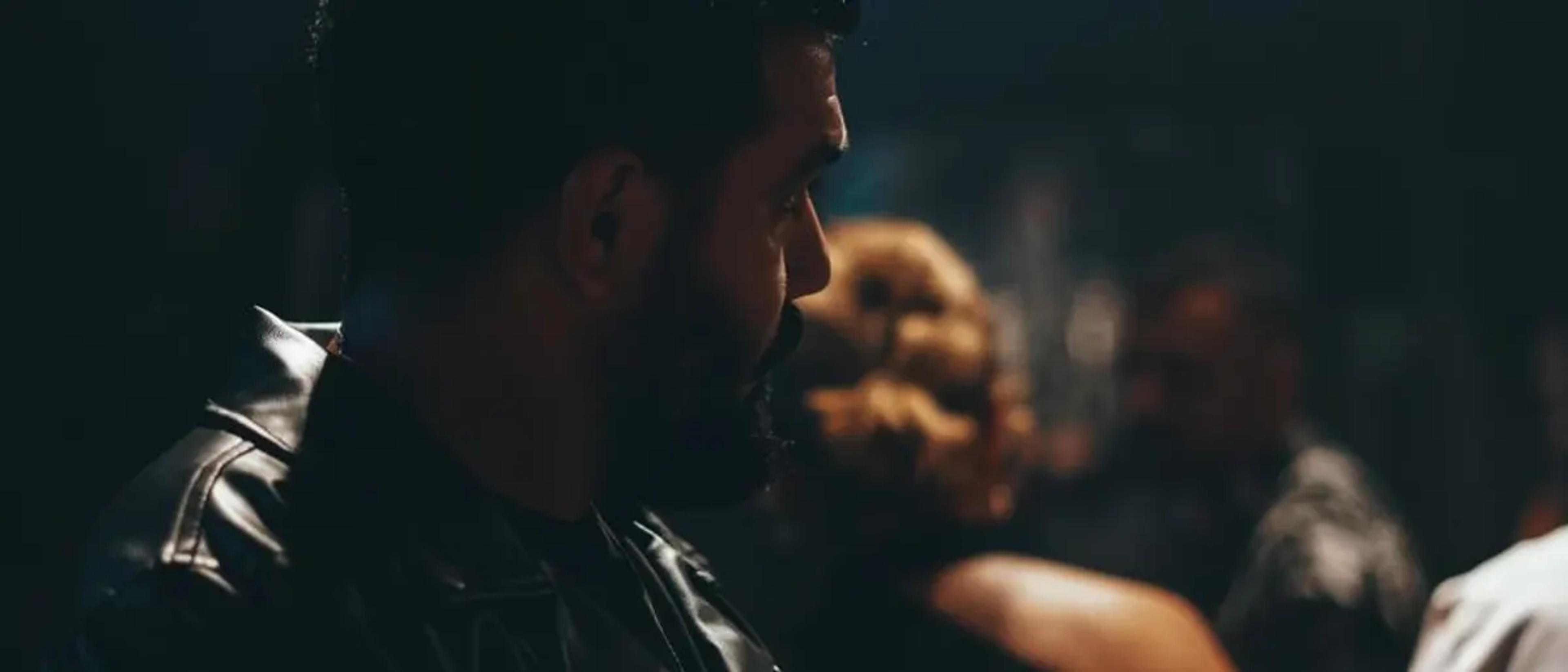 Bearded man in a black leather jacket in a dark, moody bar