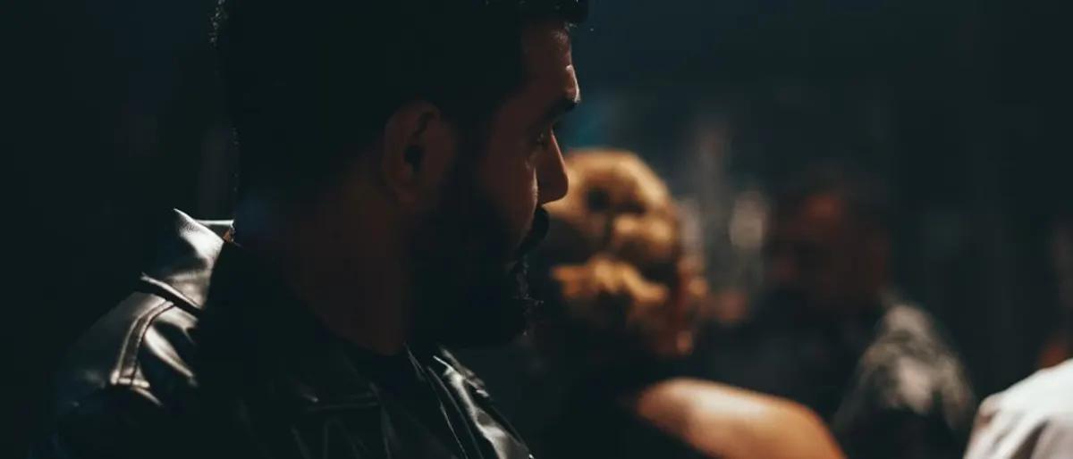 Bearded man in a black leather jacket in a dark, moody bar