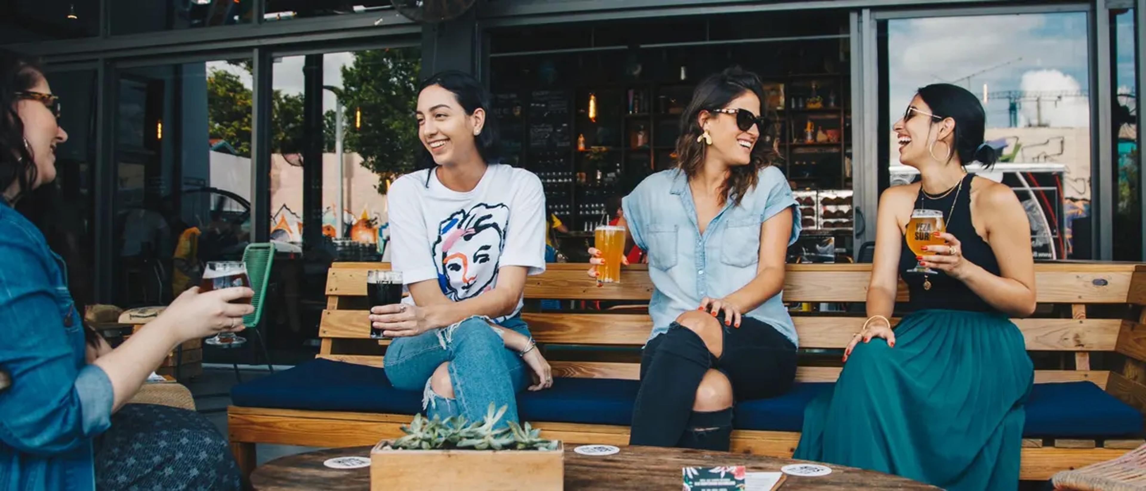 Group of women hanging out with drinks on a bench at a friendly neighborhood bar