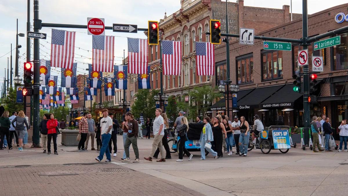 People crossing a downtown Denver intersection at Larimer Square, lined with Colorado state flags