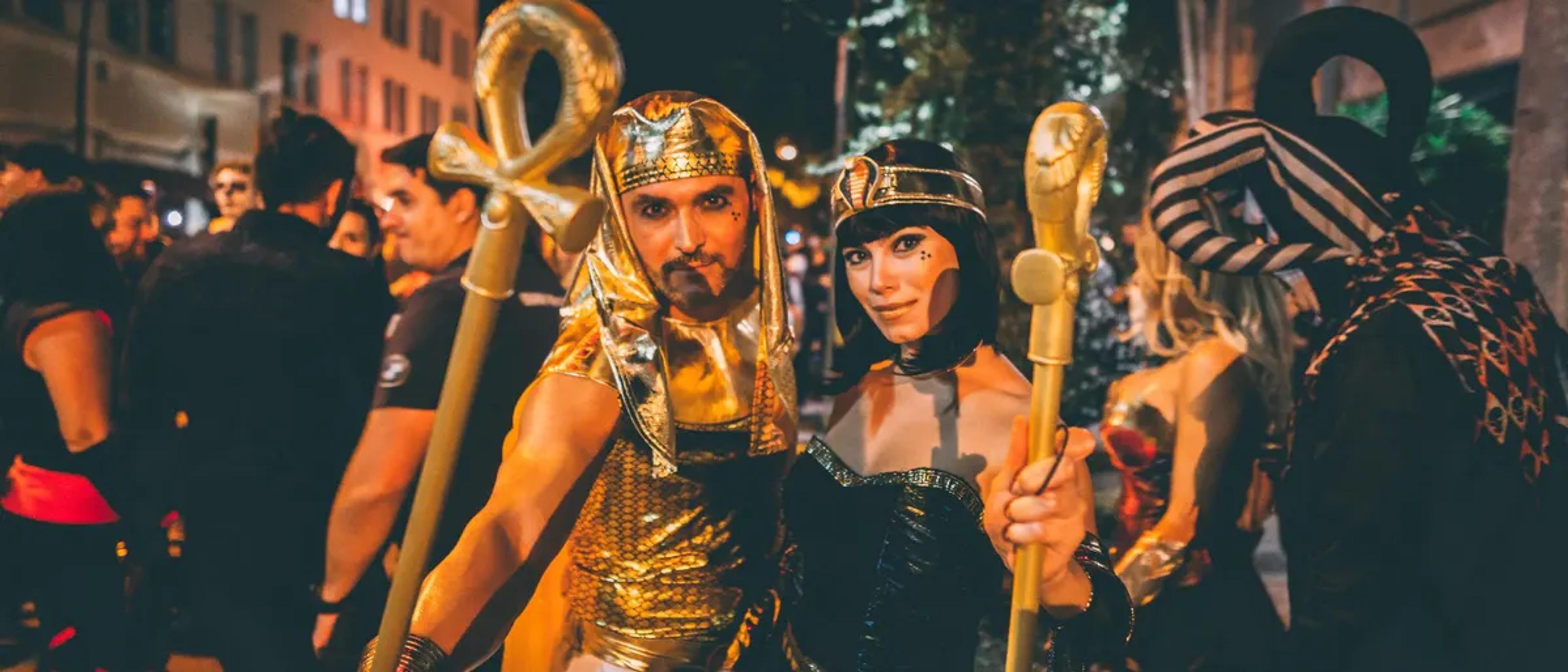 Costumed revelers including an Egyptian-themed pair at a huge nighttime Halloween street party