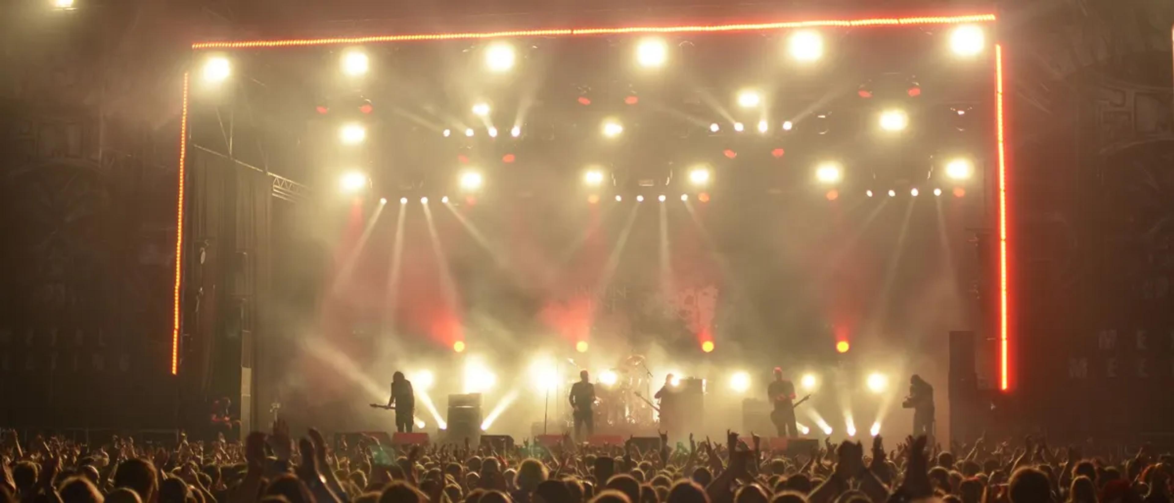 Festival crowd with hands raised under warm golden stage lights at a season-closing party