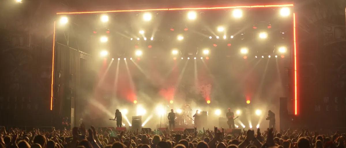 Festival crowd with hands raised under warm golden stage lights at a season-closing party