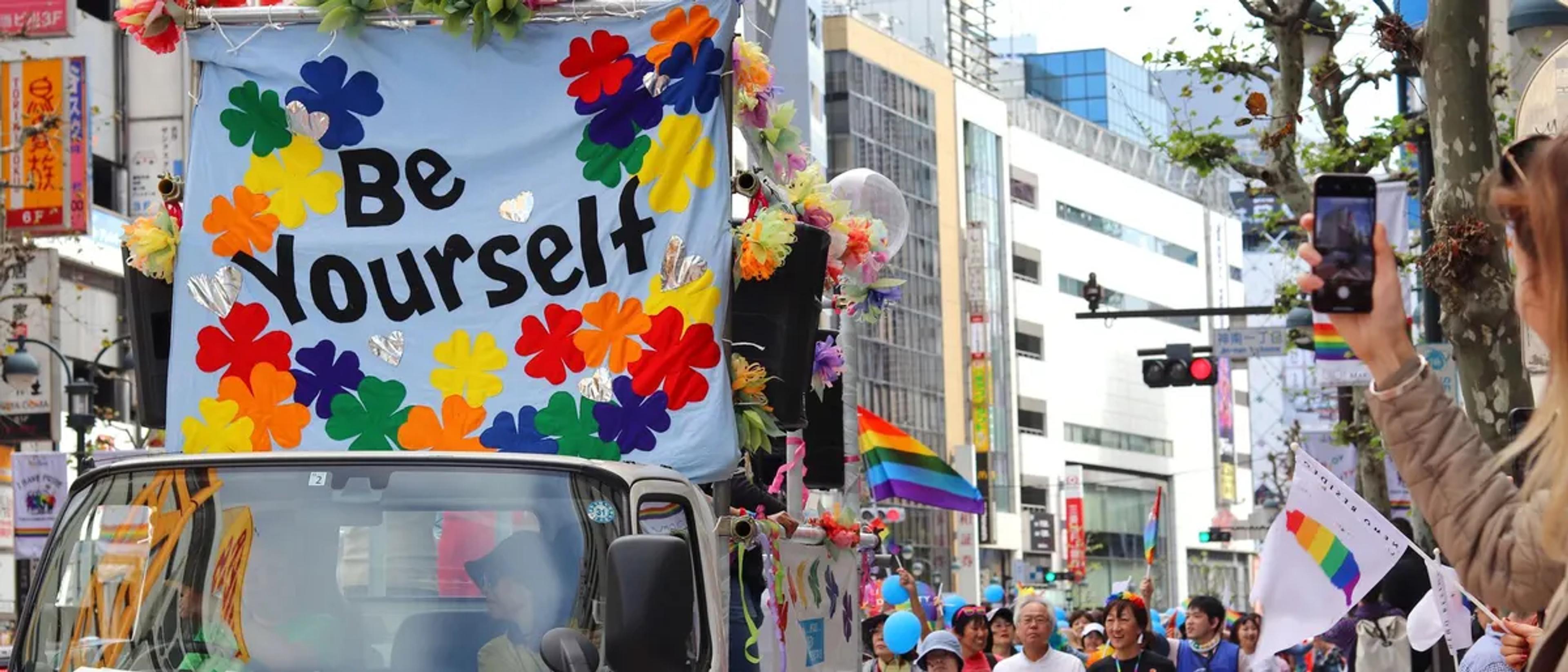 A Tokyo Rainbow Pride parade float with a Be Yourself sign and rainbow flags in Shibuya