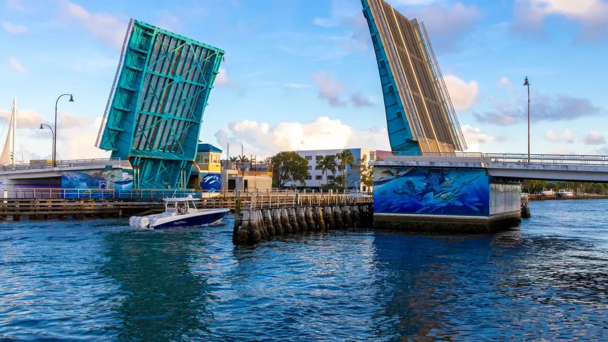 A boat passing through an open blue drawbridge on a Fort Lauderdale waterway