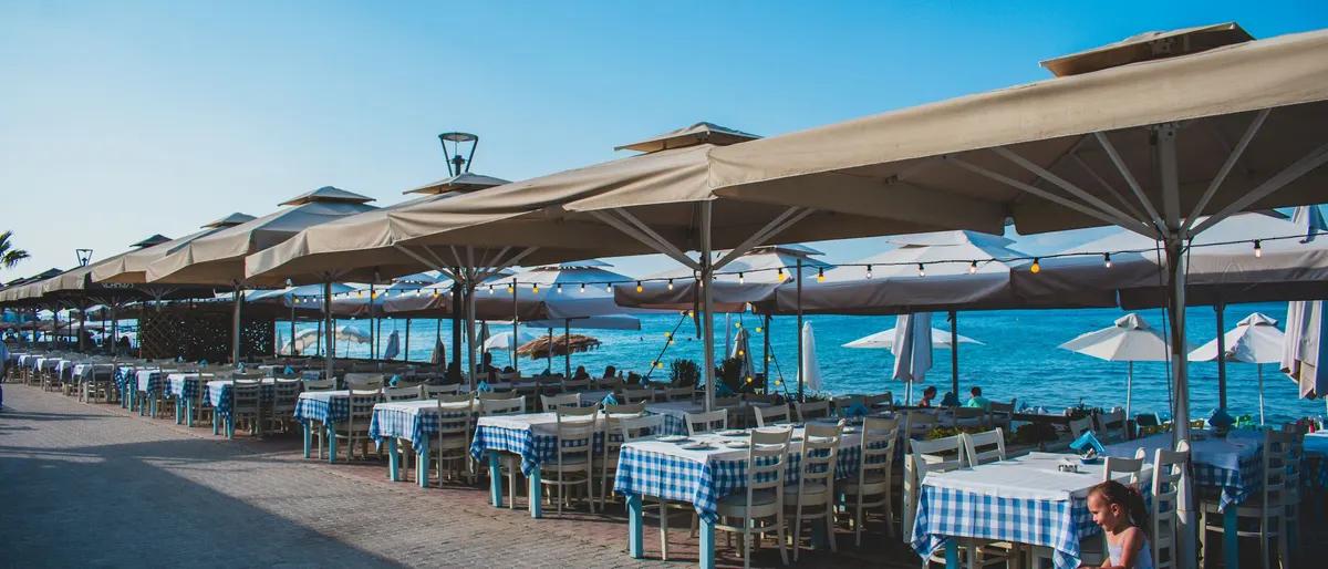 Rows of seaside restaurant tables under umbrellas beside the water