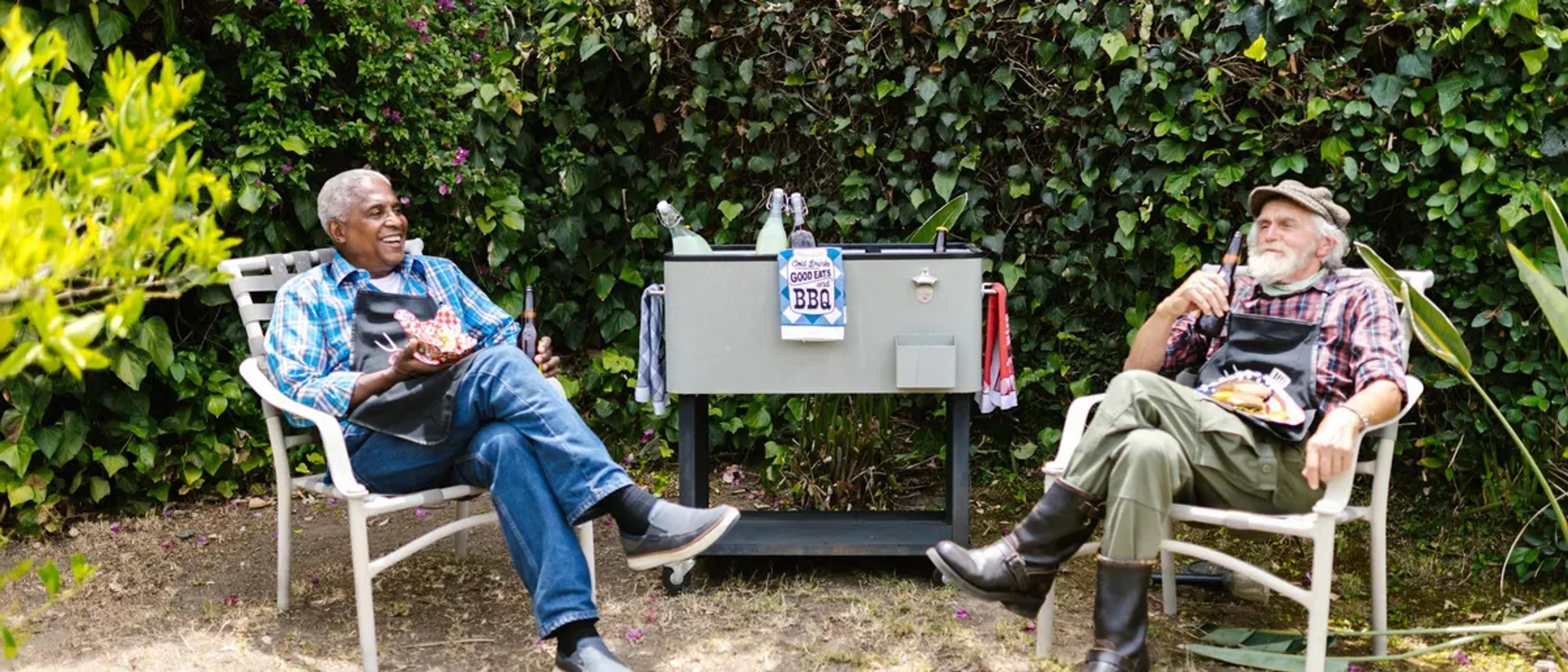 Two older men relaxing in garden chairs at a backyard barbecue