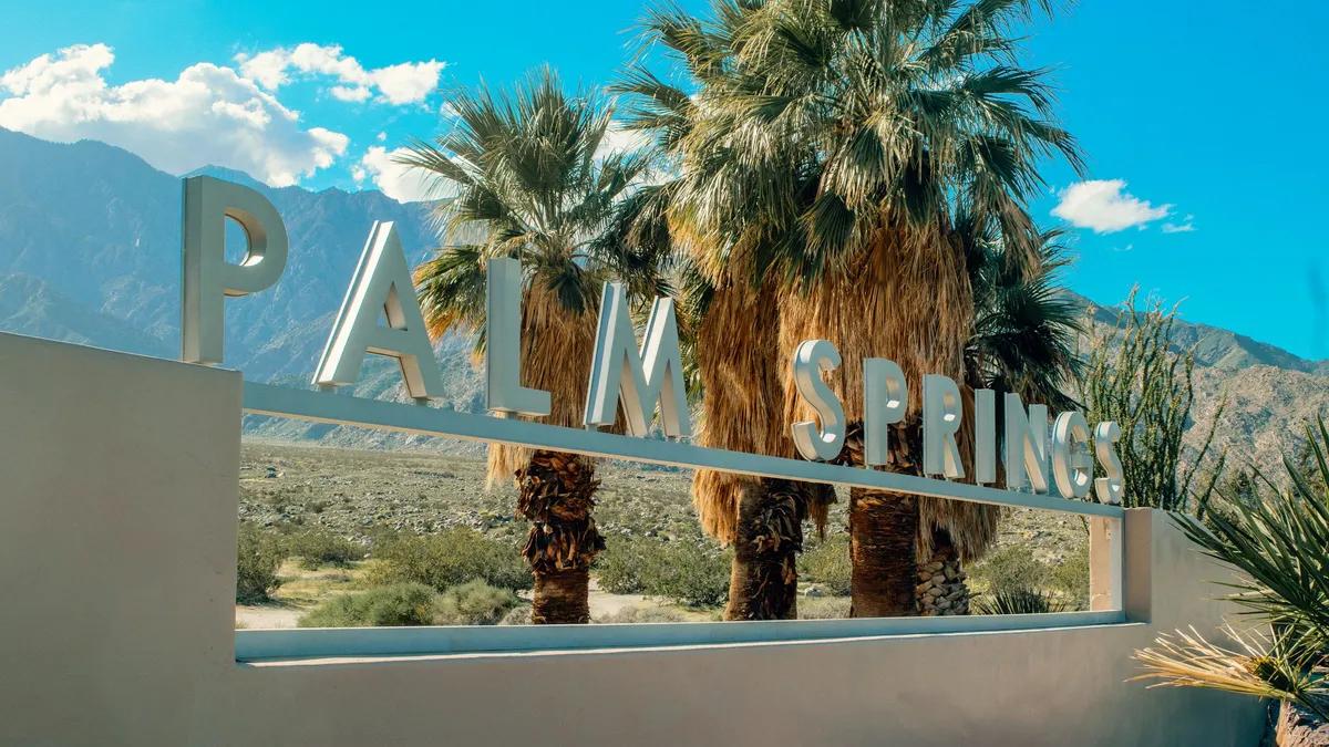 The Palm Springs city sign in front of palm trees and the San Jacinto Mountains under a clear blue sky