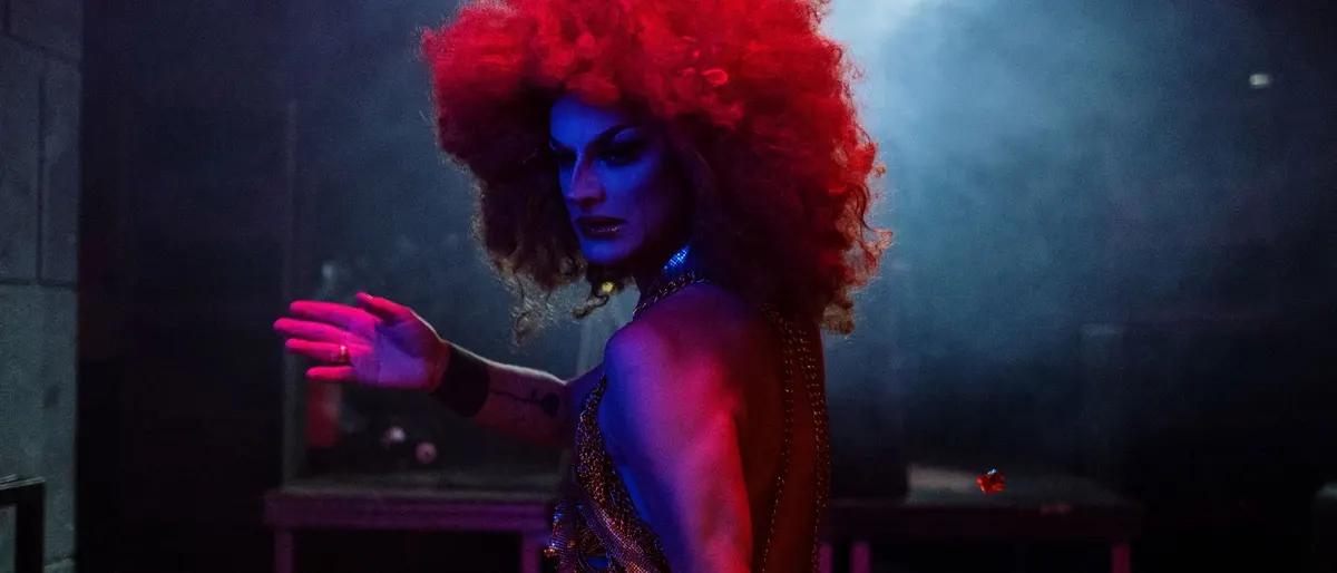 Drag performer with a red wig under dramatic stage lighting