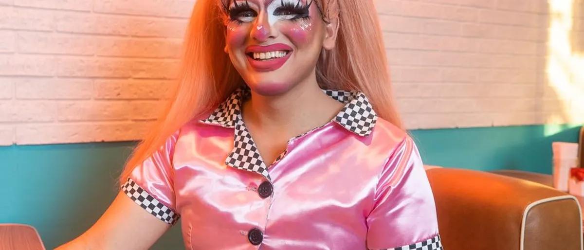 Drag performer smiling brightly in a pink diner outfit at a lively brunch