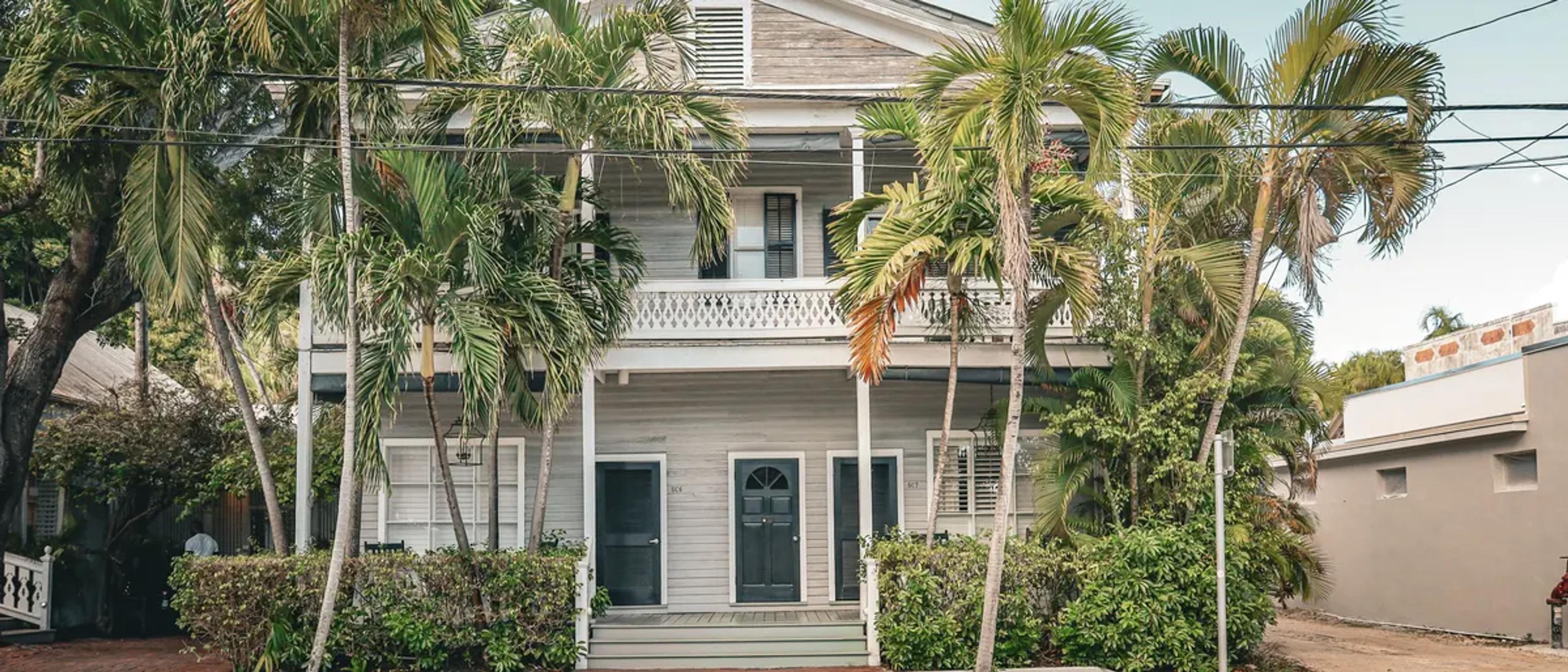 A white Conch-style house with a wraparound porch under palm trees on a Key West street