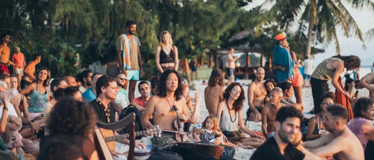 Outdoor daytime crowd dancing in the sun at a waterfront beach gathering