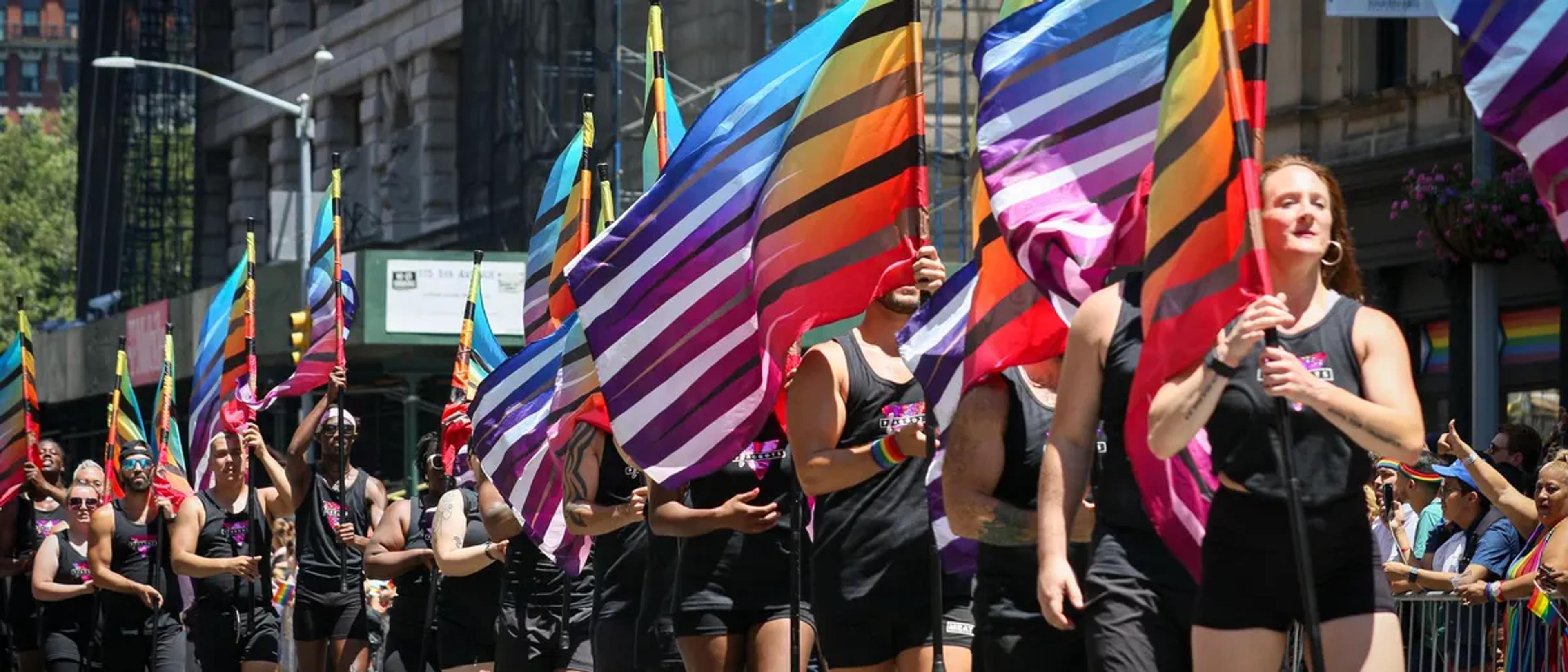 Marchers carrying large rainbow flags down a city street during a Pride parade