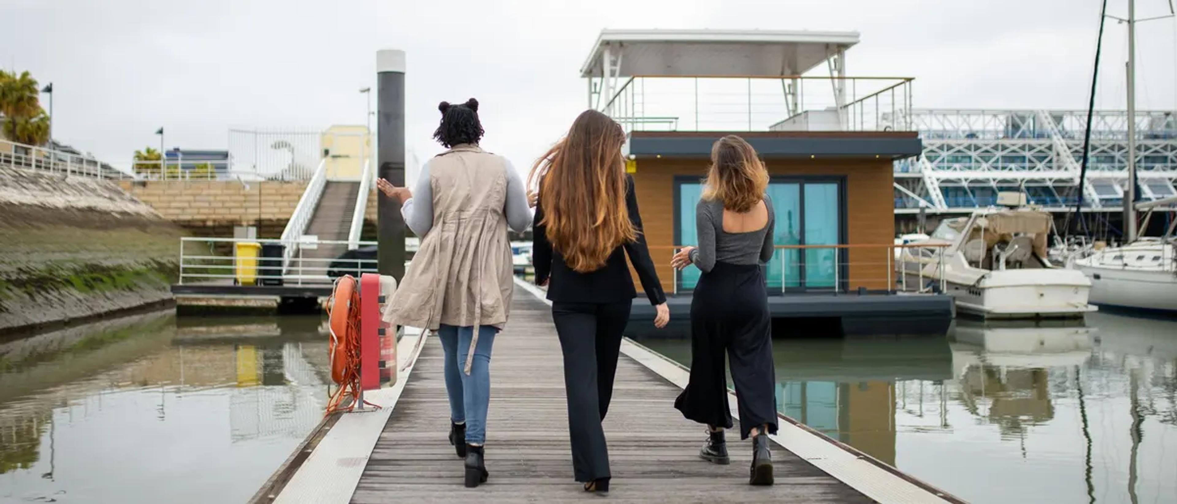 Three women walking along a marina dock toward the boats