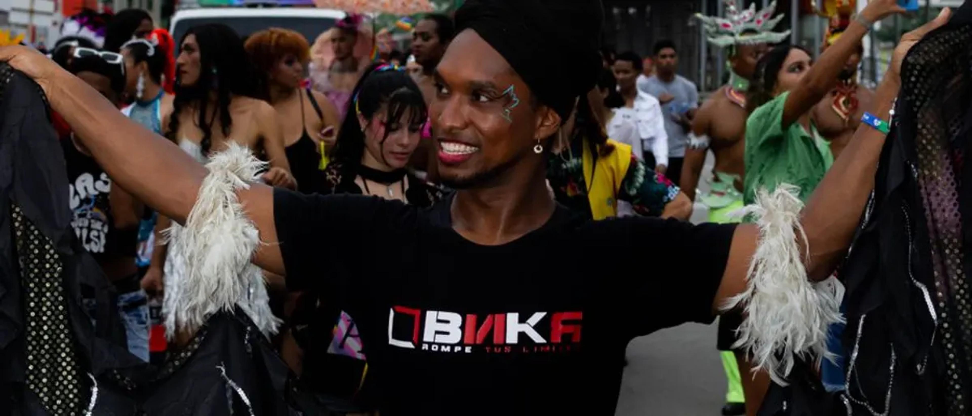 A Black reveler celebrating Pride with rainbow pom-poms and arms thrown wide