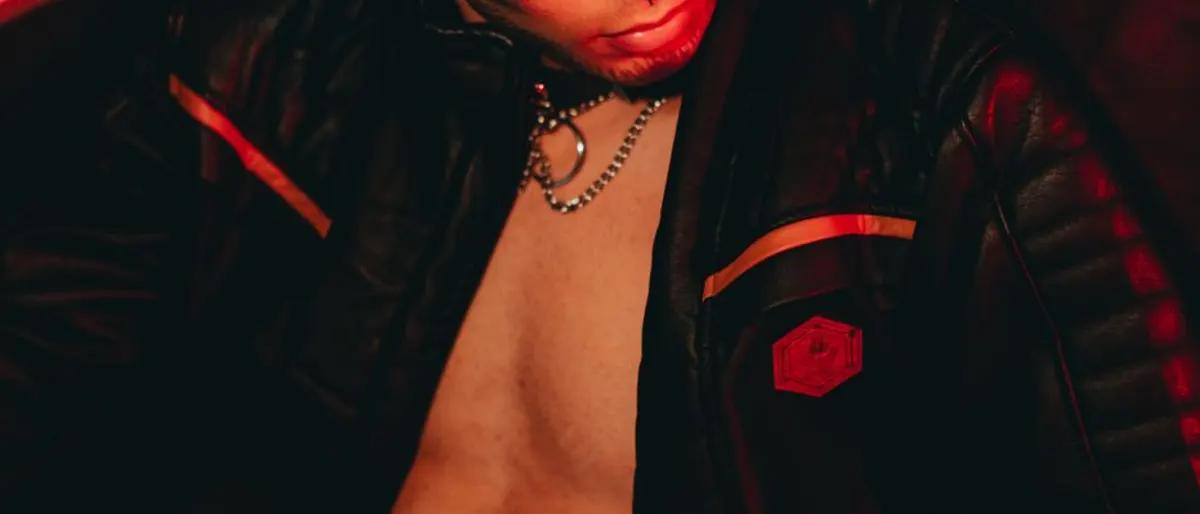 Man in an open black leather jacket with a chain necklace under red light