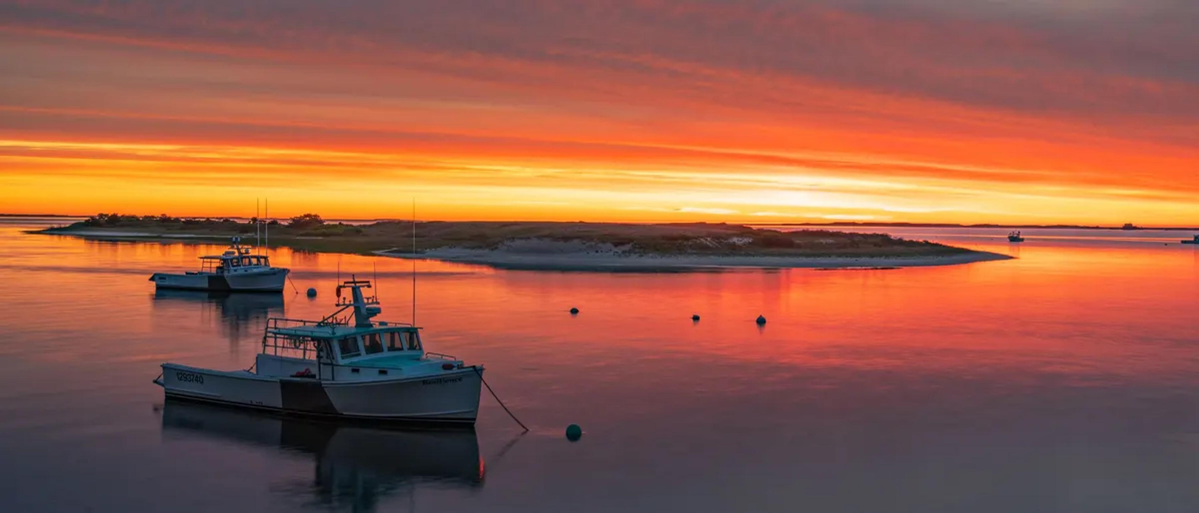 Fiery orange sunset over a Cape Cod harbor with anchored fishing boats