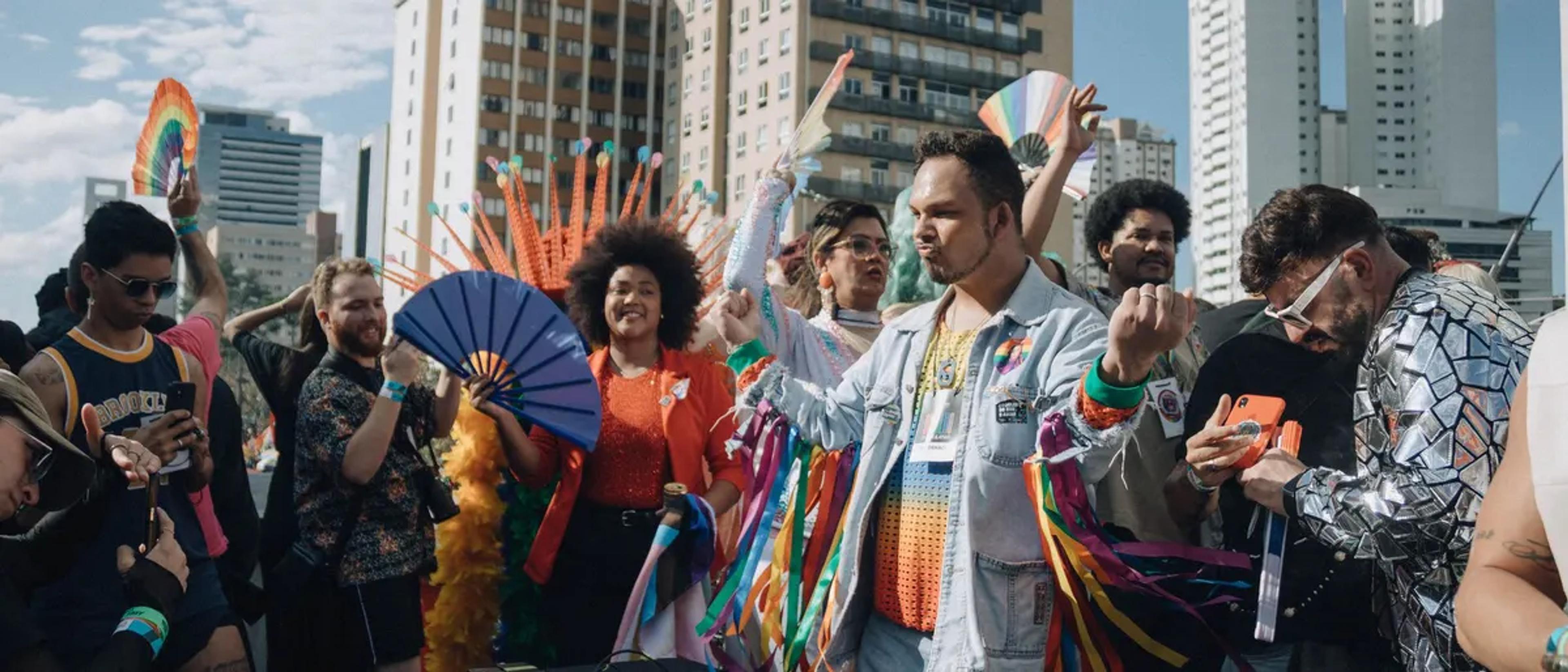 A joyful, diverse group celebrating Pride with hand fans and rainbow streamers