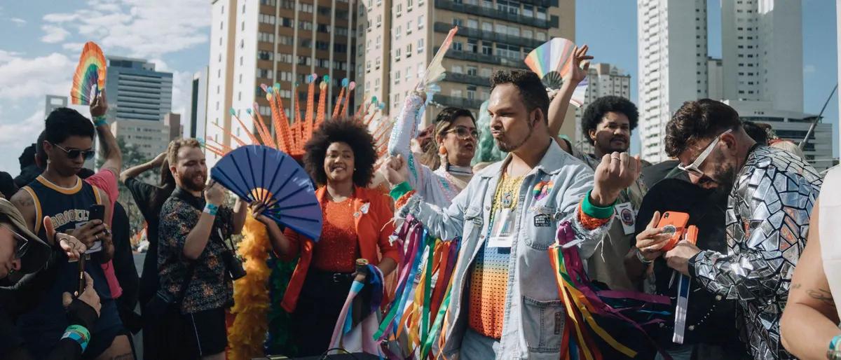 A joyful, diverse group celebrating Pride with hand fans and rainbow streamers