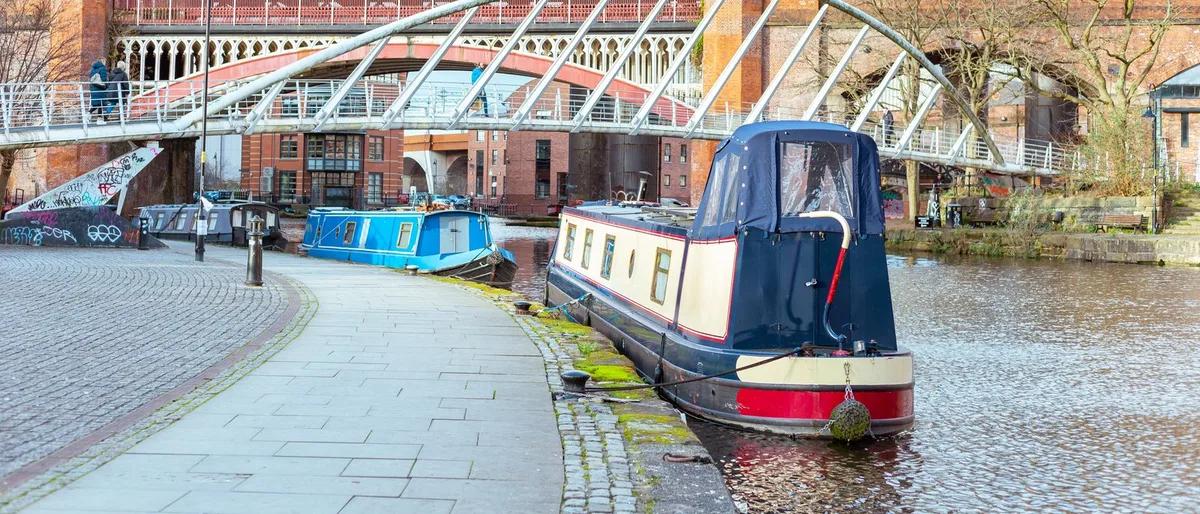Narrowboats moored on a Manchester canal beneath Victorian railway bridges